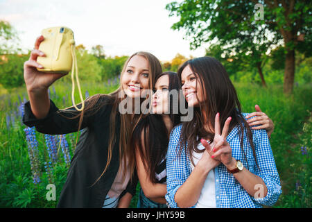 Trois filles culottes blonde and brunette taking self portrait sur un appareil polaroid et souriant à l'extérieur. Les filles s'amuser ensemble dans le parc. Banque D'Images