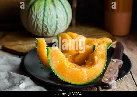 Organique mûres entières et tranchées avec cantaloup juteux pâte orange foncé, assiette, couteau, planche à découper en bois rustique, cuisine intérieur, ambiance chaleureuse Banque D'Images