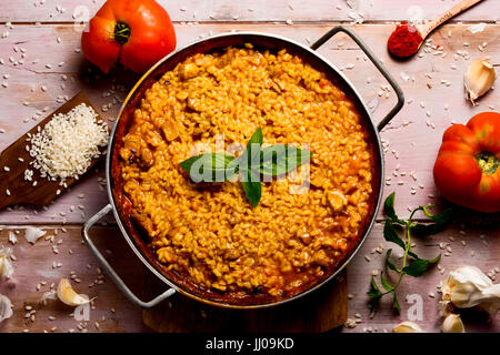 Capture d'un grand angle d'un poulet espagnol paella dans une paellera, la paella pan, et quelques ingrédients pour la préparer sur une table en bois rustique Banque D'Images