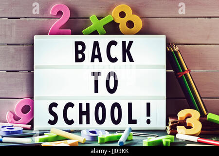 Le texte retour à l'école dans une lightbox sur un fond de bois rustique, entouré d'un nombre à trois dimensions et des craies et crayons de couleur Banque D'Images