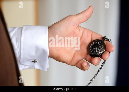 Un homme habillé avec élégance vérifie le temps à l'aide d'une montre de poche attachée à son gilet avec une chaîne. La montre a un visage noir et des chiffres romains blancs Banque D'Images