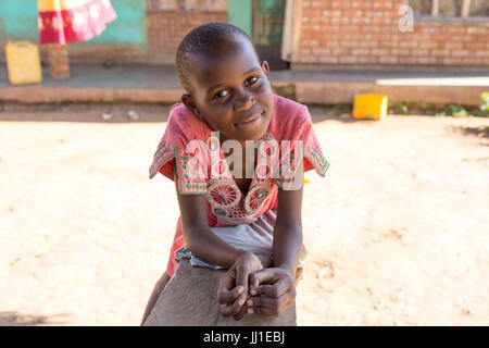 Un enfant de 9 ans smiling ougandaise appuyée sur un banc et regardant la caméra Banque D'Images