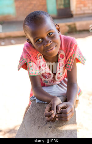 Un enfant de 9 ans smiling ougandaise appuyée sur un banc et regardant la caméra Banque D'Images