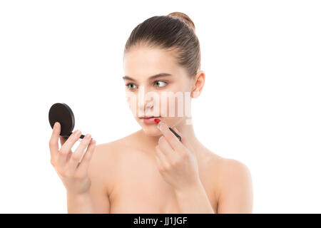 Jeune femme brune avec un visage propre appliquer le rouge à lèvres à l'aide d'un miroir. Isolé sur fond blanc. Banque D'Images