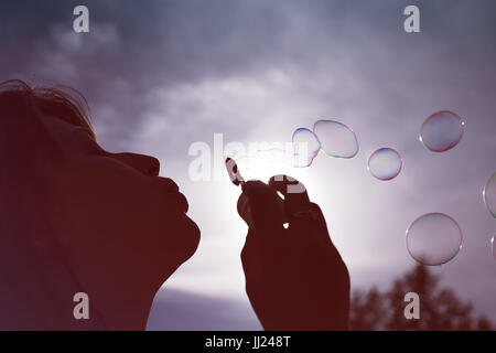 Low angle vue rapprochée de la silhouette d'une femme faisant des bulles contre un ciel bleu ensoleillé. Banque D'Images