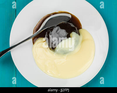 Au caramel dessert servi avec crème anglaise chaude against a blue background Banque D'Images