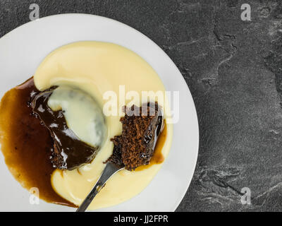 Au caramel dessert servi avec crème anglaise chaude contre un arrière-plan en ardoise noire Banque D'Images