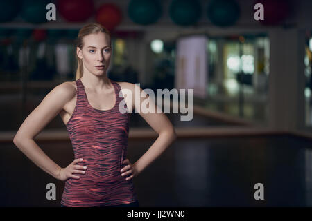 Portrait de trois quart corps athletic young woman posing in gym avec les mains sur les hanches Banque D'Images