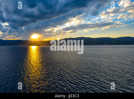 Le soleil brille sur un bateau au coucher du soleil le long de la Côte sicilienne de l'Italie Banque D'Images