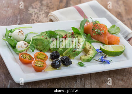 Assiette de tranches d'avocat et saumon griller le pain d'épices et de mozzarella, tomates bourrache torchon avec olives noires et décor sur fond de bois Banque D'Images