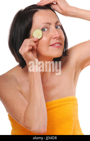 Cheerful mature woman holding morceau de concombre à l'avant de l'œil et sourire. Traitement spa naturel. Isolé sur fond blanc Banque D'Images