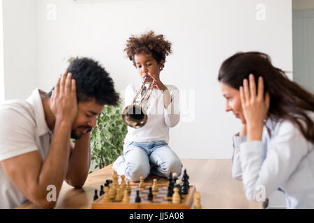 La mère et le père essayant de jouer aux échecs pendant que leur enfant joue trompette