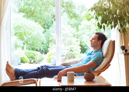 Homme heureux de vous détendre dans une chaise longue à la maison, bien-être, relaxation d'arrière-plan Banque D'Images