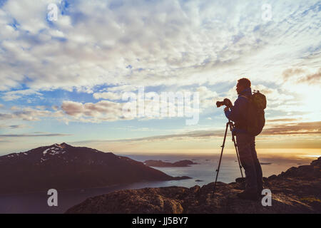 Photographe avec trépied prendre panorama de belle nature paysage en Norvège au coucher du soleil, la silhouette de l'homme avec l'appareil photo dans les fjords Banque D'Images