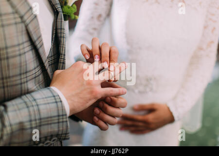 La vue en gros plan des mains de la mariée de mettre l'anneau de mariage sur le doigt du marié. Banque D'Images