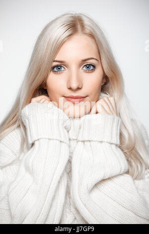 Belle jeune femme blonde vêtue de blanc grand pull en cachemire sur fond gris Banque D'Images