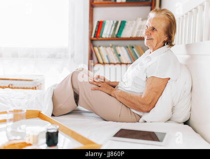 Happy elderly woman having breakfast in bed, tout en utilisant son tablet Banque D'Images