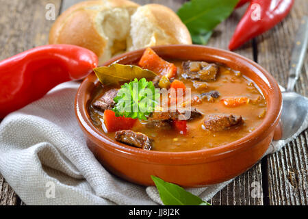 Soupe de goulash hongrois chaud servi dans un bol en céramique avec un rouleau frais Banque D'Images