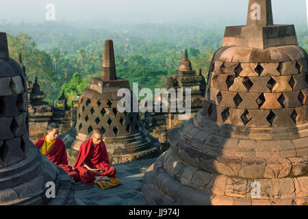 Robe rouge moines priant au lever du soleil sur le site du patrimoine mondial buddist temple Borobudur. Banque D'Images