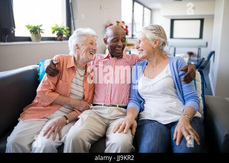 Smiling senior man sitting avec bras autour de sur les femmes des amis sur canapé à la maison de soins infirmiers Banque D'Images