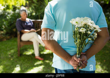 La mi-section de man se cachant derrière des fleurs retour au jardin Banque D'Images