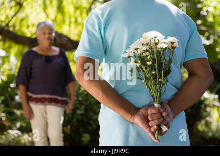 La mi-section de man se cachant derrière des fleurs retour au jardin Banque D'Images