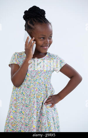 Smiling businesswoman with hand on hip parlant au téléphone contre wall in office Banque D'Images