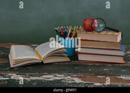 Pile de livres avec loupe, apple et porte-stylo sur table en bois Banque D'Images