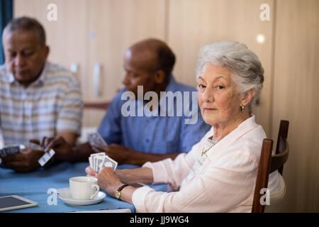 Portrait of senior woman sitting avec des amis tout en jouant aux cartes à la maison de soins infirmiers Banque D'Images