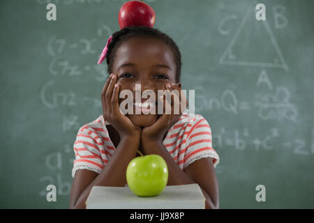 Portrait de lycéenne assis à la pomme sur sa tête contre le tableau Banque D'Images