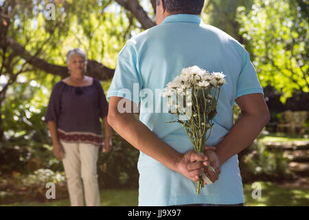 La mi-section de man se cachant derrière des fleurs retour au jardin Banque D'Images