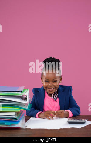 Portrait of smiling businesswoman typing while sitting at desk contre pink wall in office Banque D'Images