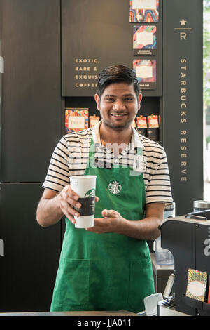 Starbucks Barista regardant la caméra en souriant, tenant une tasse de café. Banque D'Images
