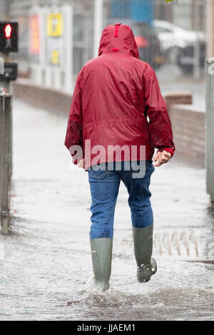 Un homme marche à travers l'eau des inondations éclair sur son chemin du retour après de fortes pluies ont causé des inondations éclair à l'A525 en été pendant le tonnerre et la foudre tempêtes qui ont frappé la région, Rhyl, au nord du Pays de Galles, Royaume-Uni Banque D'Images