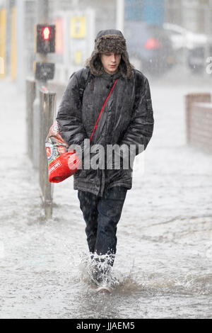 Un homme marche à travers l'eau des inondations éclair sur son chemin du retour après de fortes pluies ont causé des inondations éclair à l'A525 en été pendant le tonnerre et la foudre tempêtes qui ont frappé la région, Rhyl, au nord du Pays de Galles, Royaume-Uni Banque D'Images