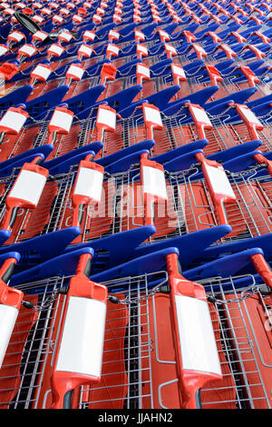 Des rangées de chariots rouges et bleus se nichaient les uns dans les autres dans un supermarché. Banque D'Images