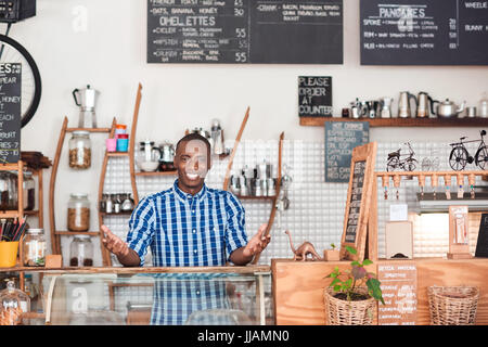 Portrait d'un jeune entrepreneur africain smiling while standing welcomingly derrière le comptoir de l'ordre de ses cafés à la Banque D'Images