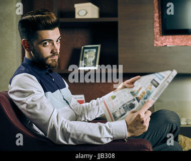 Jeune homme lisant le journal dans le salon Banque D'Images