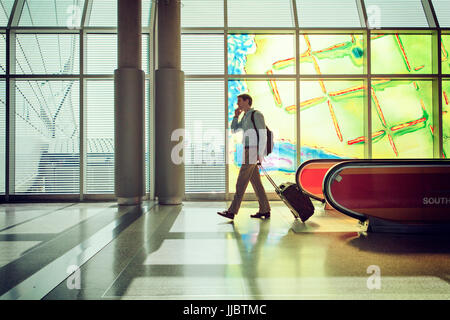 Man talking on cellphone et en tirant un sac dans un aéroport. Banque D'Images