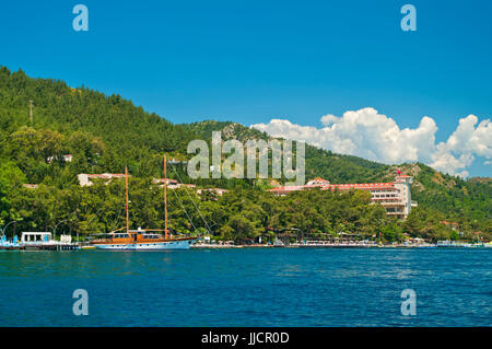 Vue d'un voilier amarré au quai en mer près de la plage de l'hôtel avec les montagnes et le ciel bleu au fond, Marmaris, Mugla, Turquie Banque D'Images