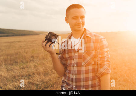 Portrait of attractive male photographe en plein air au coucher du soleil. Jeune homme avec une caméra en main Banque D'Images