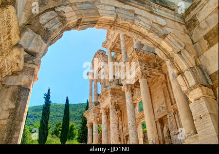 Vue de la bibliothèque de Celsus à façade et colline verte avec des cyprès et bleu ciel à travers arch à Éphèse, Turquie Banque D'Images