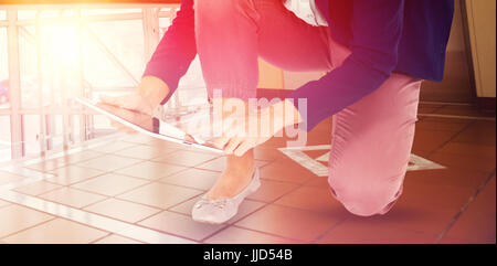 La section basse de businesswoman à genoux pendant l'utilisation de tablette numérique contre hall d'accueil avec ascenseur Banque D'Images