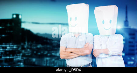 Couple wearing sacs en papier sur la tête contre les bâtiments illuminés en ville contre sky Banque D'Images