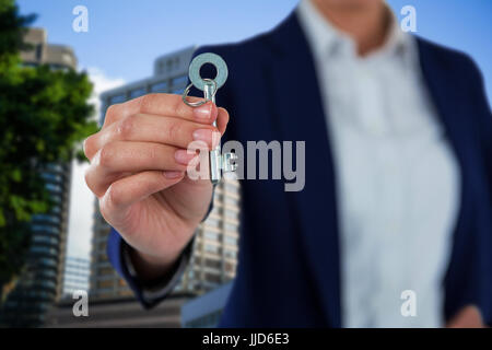 Mid section of businesswoman showing new house key contre belle cityscape contre ciel clair Banque D'Images
