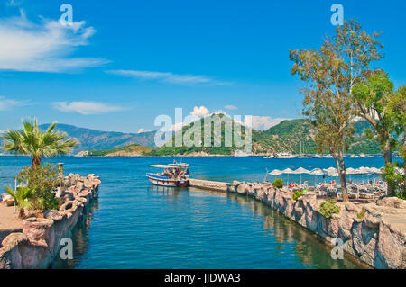 Petit bateau touristique sur icmeler pier en mer Egée bay avec des palmiers à foeground et les montagnes à l'arrière-plan, Marmaris, Turquie Banque D'Images