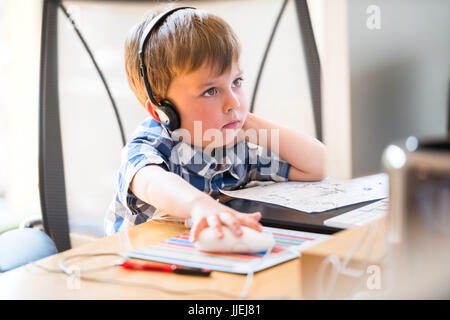 Un écolier étudie à la maison et fait des devoirs à l'école à l'écoute de la leçon avec des écouteurs. Formation à distance en ligne. Banque D'Images