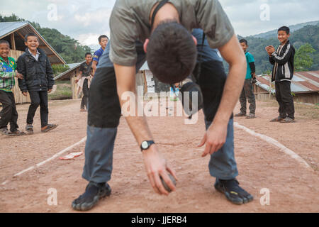 Robert Hahn joue aux boules (pétanque) avec les étudiants dans un pensionnat, en plaisantant de lancer la balle entre ses jambes, à Ban Tang, le Laos. Banque D'Images