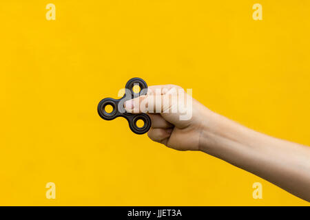 Human hand holding black fidget spinner sur fond jaune. Banque D'Images