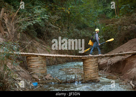 Robert Hahn marche à travers un pont de bambou tressé sur un affluent de la rivière Nam Ou pour entrer Ban Huay Phouk, Laos. Banque D'Images